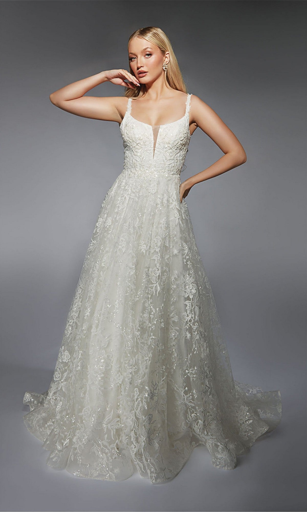 A woman poses against a plain gray background wearing the Alyce 7123 long formal dress in ivory, featuring a floor-length lace design with a fitted, sequin-embellished bodice and wide straps.